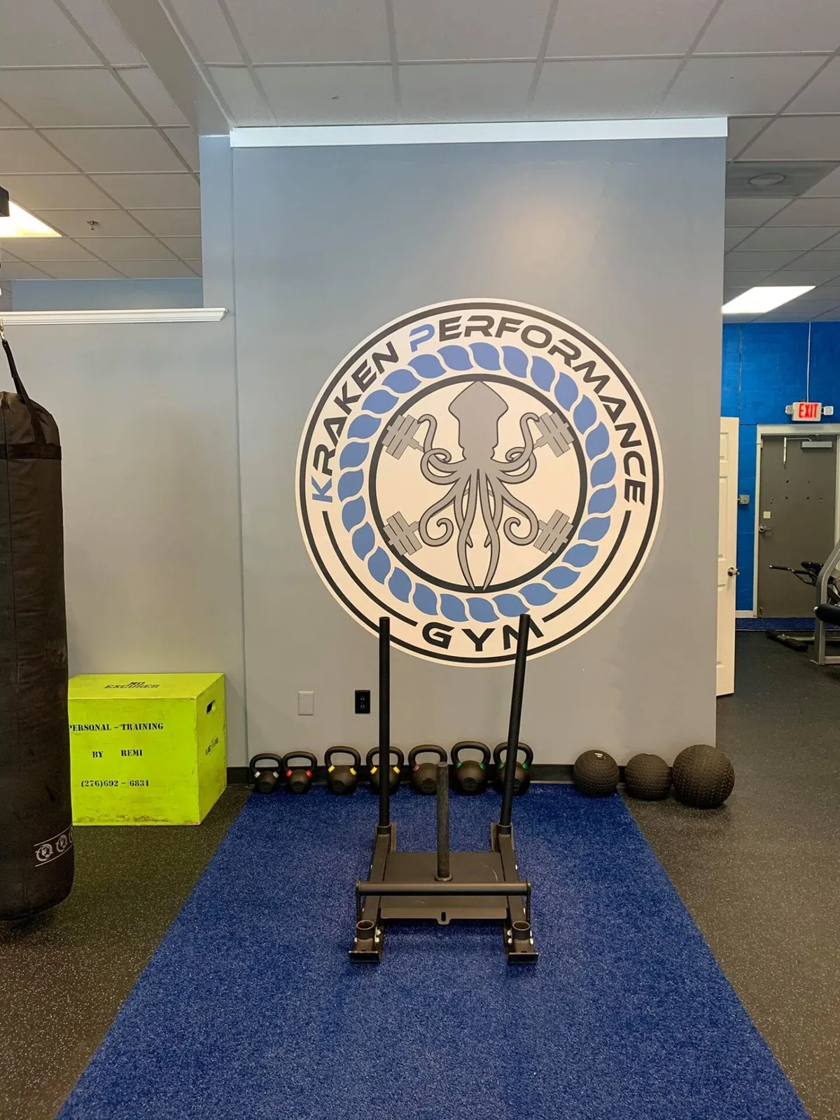 Inside Kraken Performance Gym, with sled and kettlebells in front of the Kraken logo wall