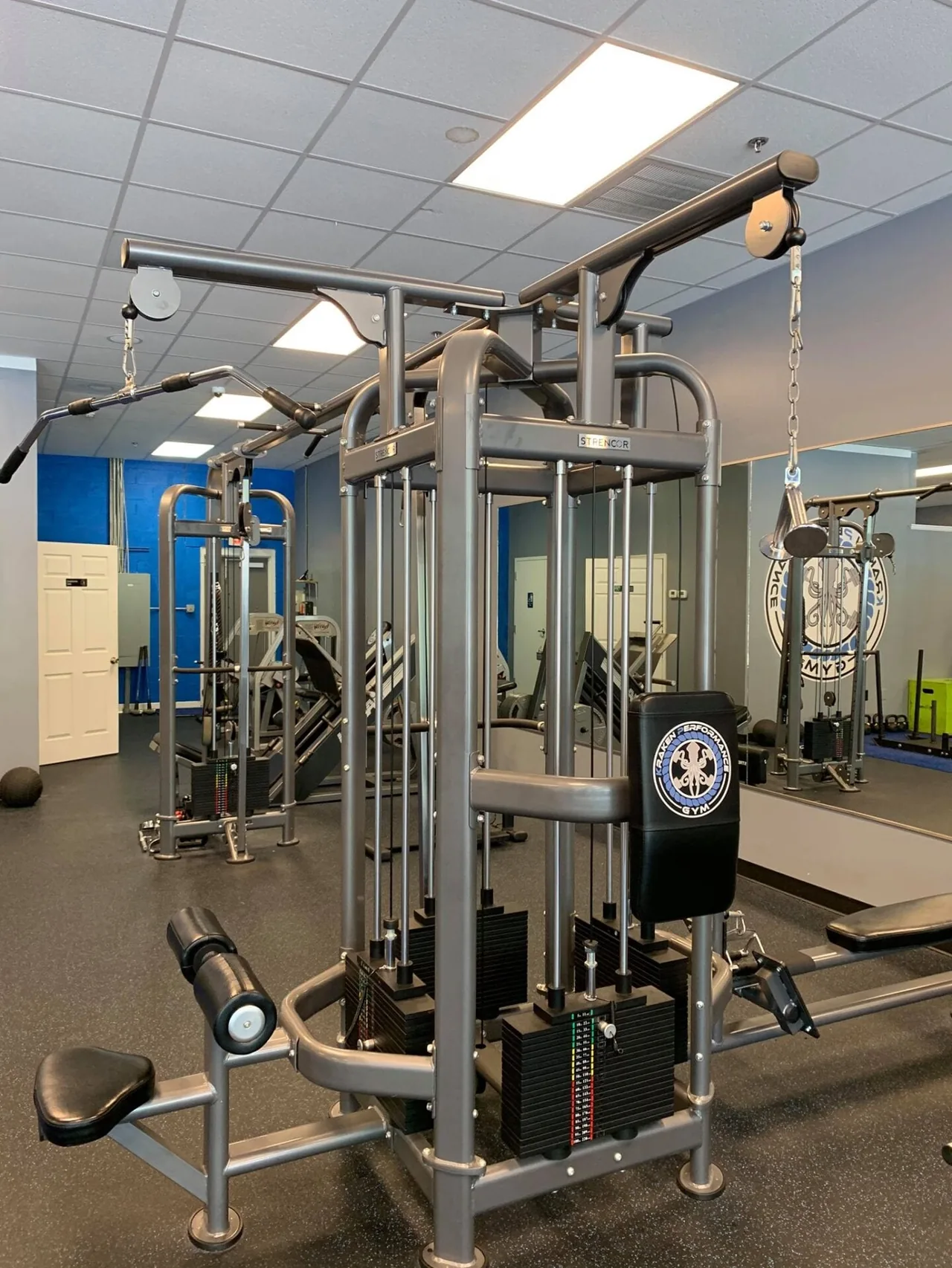 Strencor cable cross-over station with a Kraken-branded pad, surrounded by additional cable machines and free-weight equipment.