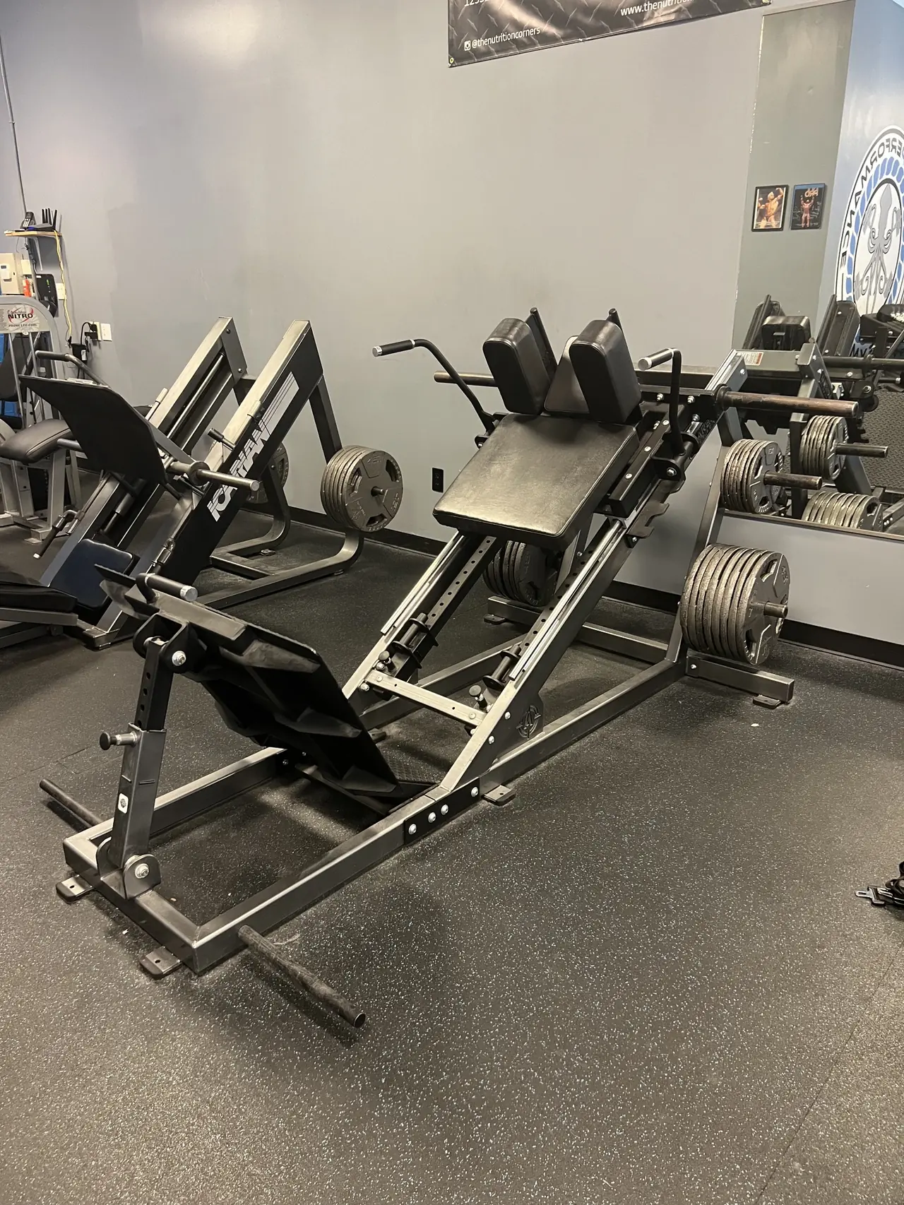 Plate-loaded hack squat and leg press pair with Olympic plates racked on the horns.